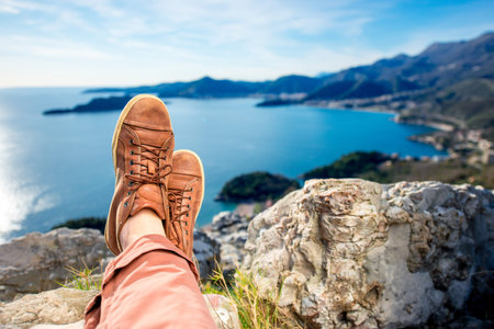 Mens legs in the brown shoes lying on the mountain on the sea scape background