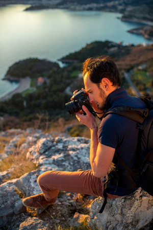 Photographer with professional photo camera and backpack on the top of the mountain on the beautiful sunset.の写真素材