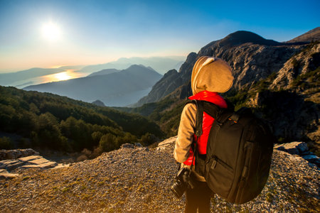 Young traveler photographer with photo camera and backpack standing on the top of mountain and...