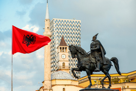 Skanderbeg monument with flag, mosque and clock tower on background in the center of Tirana city, Albania.の写真素材