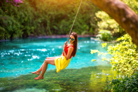 Happy young woman swinging with bungee above the river in the forest