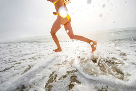 Sexy woman in yellow bikini running and having fun on the beach splashing water.