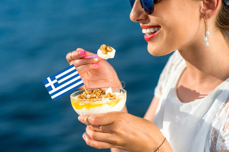 Smiling woman eating traditional greek yogurt with nuts and honey outdoors on blue sea background