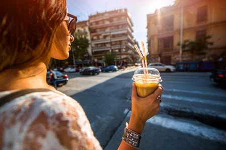 Young woman walking on the street with take away coffee  in the transparent cup in the cityの写真素材