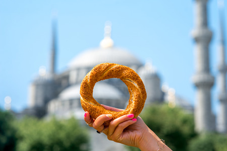 Holding turkish bagel with Blue Mosque on background. Traditional turkish street food.の写真素材