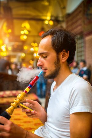 Man smoking turkish hookah in the cafe with coloful lamps on background in Istanbul, Turkeyの写真素材