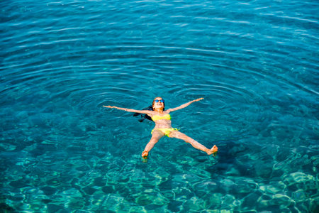 Young woman in yellow swimsuit swimming and relaxing in the blue water sea. Top view with copy space