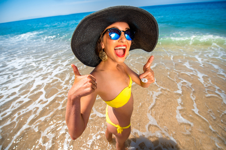 Young woman in yellow swimsuit and big hat having fun on the beachの写真素材