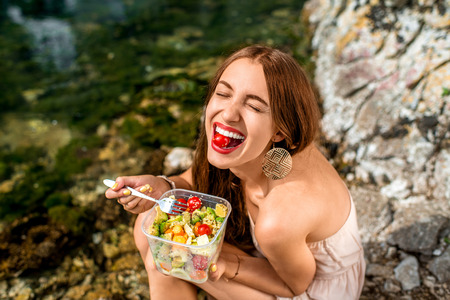 Woman eating healthy salad from plastic container near the river Woman eating healthy salad from plastic container near the river