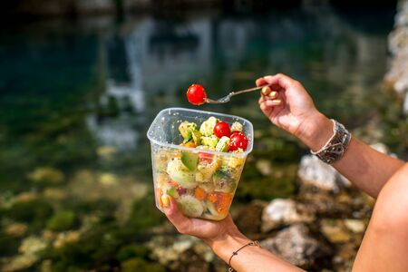 Woman eating healthy salad from plastic container near the riverの写真素材
