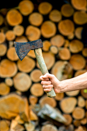 Male hand holding an ax on a stack of firewood backgroundの写真素材