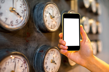Female hand holding phone with white screen and metal clocks on background. Time phone application...