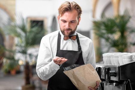 Handsome barista in classical uniform checking coffee beans at the cafe terraceの写真素材