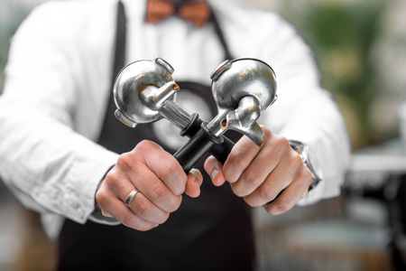 Barista in uniform holding coffee machine holders. Close up view focused on handsの写真素材