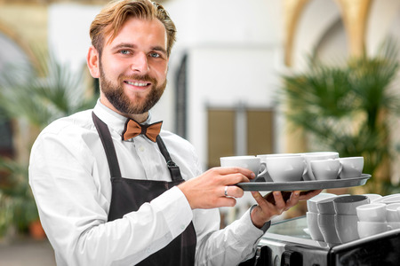 Portrait of handsome smiling barista with coffee cups in the cafeの写真素材