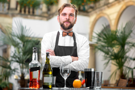 Portrait of handsome barman in uniform with bottles and shaker at the restaurantの写真素材