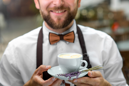 Elegant barista holding cup with lavender cappuccino. Closeの写真素材