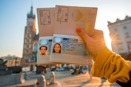 Female hands holding Ukrainian passports with Shengen visas on the Krakow city center background. Traveling to Europe from Post-Soviet countries conceptの写真素材