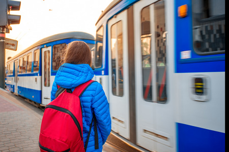 Young female tourist in blue jacket with backpack on the station with blue tram on backround. Motion effectの写真素材
