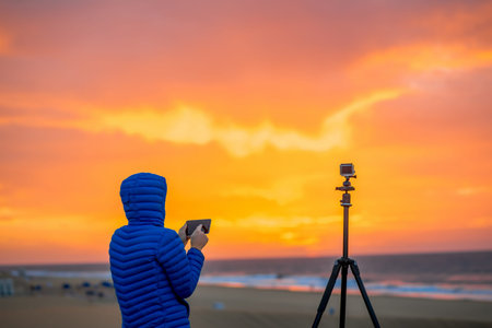Young female photographer filming time lapse video with phone and small action camera on the tripod on the early morningの写真素材