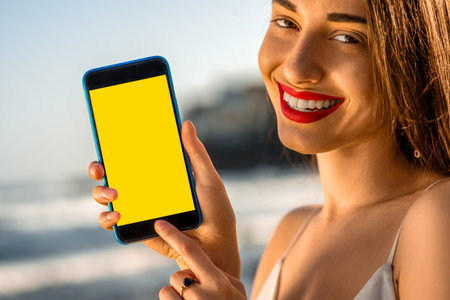 Young and pretty woman showing smartphone with yellow screen on the beautiful rocky seacoast.