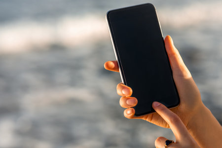 Female hands holding smartphone on the blurred sea background