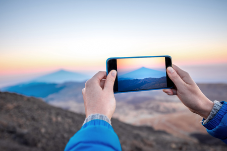 Photographing with smartphone beautiful volcanic landscape with big shadow on the ocean on the sunsetの写真素材