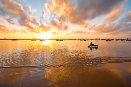 Fiserman with boat in the ocean near the sandy beach on the sunriseの写真素材