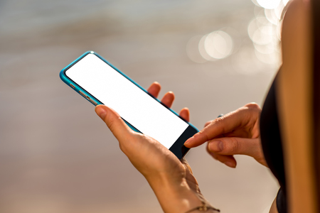 Female hands holding smartphone with white screen on the blurred water backroundの写真素材