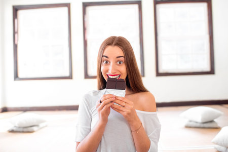 Young and smiling woman eating black chocolate without worrying about calories and weight sitting in...