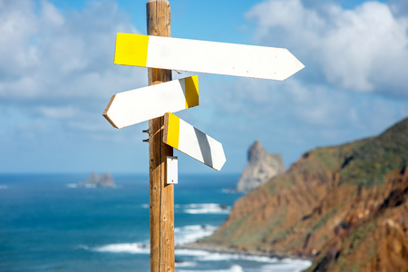 Wooden road sign with empty boards on the ocean and mountains backroundの写真素材