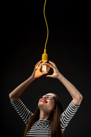 Young female inventor looking on the illuminated retro lamp on the dark backgroundの写真素材
