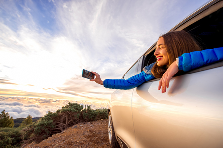 Young woman photographing with smart phone beautiful cloudscape looking out the car window above the clouds on the sunriseの写真素材