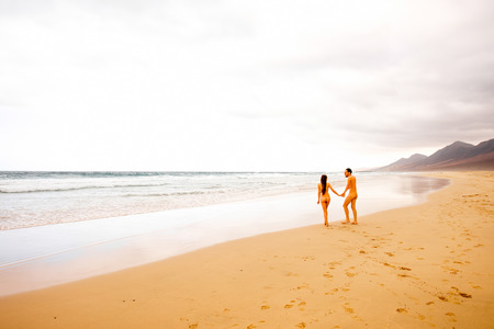Naked couple walking beautiful sandy beach with mountains on the background. General plan, rear view with copy spaceの写真素材
