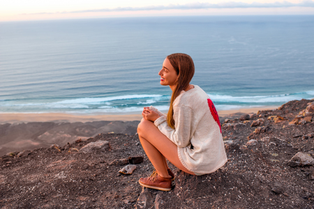 Young woman enjoying nature sitting on the mountain with ocean on background on Fuerteventura island in Spainの写真素材