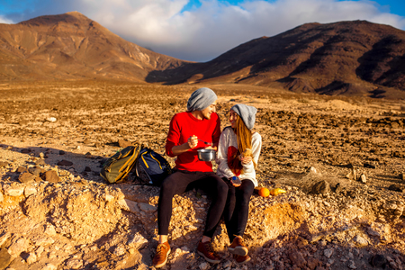 Young couple travelers eating healthy food from cooking pan sitting on the ground on desert mountain landscape background.の写真素材