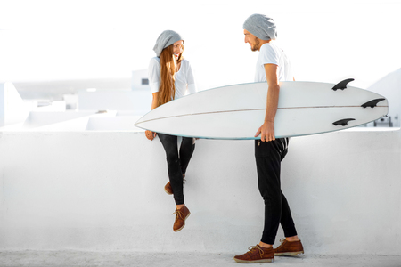 Young couple dressed alike in white t-shirts and hats enjoying summer vacations with surfboard on the roof top in the morningの写真素材