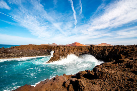 Los Hervideros rocky coast with wavy ocean and volcanos on the background on Lanzarote island in...