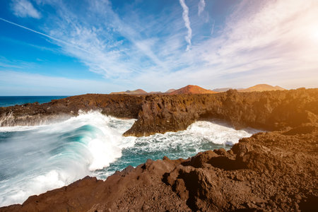 Los Hervideros rocky coast with wavy ocean and volcanos on the background on Lanzarote island in...