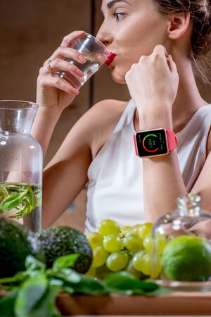 Close-up portrait of a young sport woman drinking water with smart watch showing calories and healthy food on the foregroundの写真素材