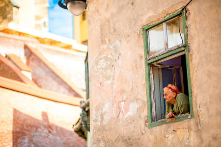 SIBIU, ROMANIA - CIRCA JUNE 2015: Elder woman looks out the window in old building in Sibiu old town...