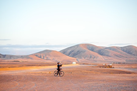 EL COTILLO, FUERTEVENTURA ISLAND, SPAIN - SIRCA JANUARY 2016: Bicycle rider makes picture of a beautiful landscape with mountains on the background near El Cotillo on Fuerteventura island.のeditorial素材