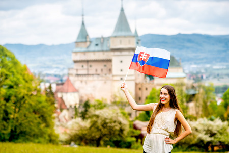 Young female tourist holding slovak flag with Bojnice castle on the background in Slovakia. Promoting tourism in Slovakiaの写真素材