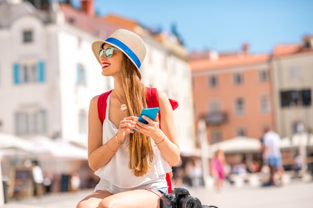 Young female traveler using mobile phone sitting on the central square in Piran old town. Traveling in Sloveniaの写真素材