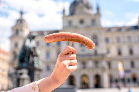Woman holding sausage on the city background with town hall building in Graz. Austrian street foodの写真素材