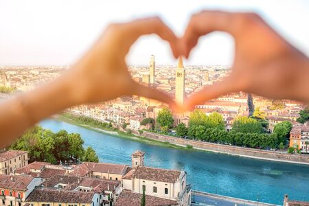 Female hands making heart shape on Verona cityscape background. Verona is famous city of love in the north of Italy.の写真素材