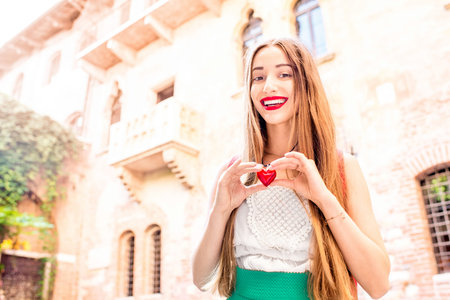 Beautiful woman holding decoration in the form of heart near Romeo and Juliet balcony in Verona. Romeo and Juliet is a romantic tragedy written by William Shakespeareの写真素材