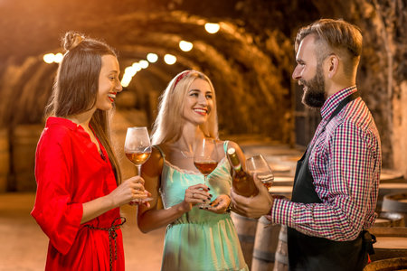 Wine degustation with sommelier or wine maker and two pretty women in colorful dresses in the old...