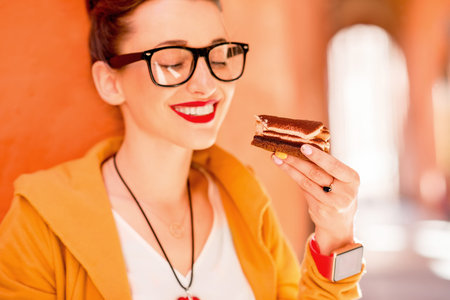 Young woman eating tiramisu, traditional italian dessert, on the street in Bologna city in Italy. Tiramisu was invented in Veneto region in Italy. Soft focus with small depth of fieldの写真素材