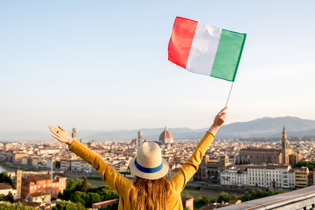 Young female traveler waving italian flag on the old town background in Florence in the morning. Promoting tourism in Italy. Back view with copy spaceの写真素材